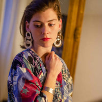 Close-up of a blonde woman wearing gold coated handmade bronze earrings and a silver bracelet