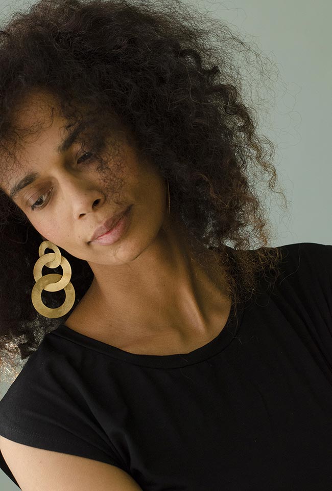 Close-up of a woman with curly hair wearing coated handmade bronze earrings