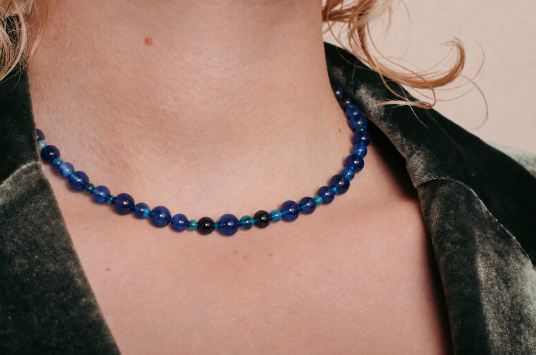 la modella indossa: Collana Blue Beads di RIMA,  composta da splendide perline in pietra naturale dalle tonalità variabili del blu, estremamente lucide e impreziosite da venature e sfumature più scure.