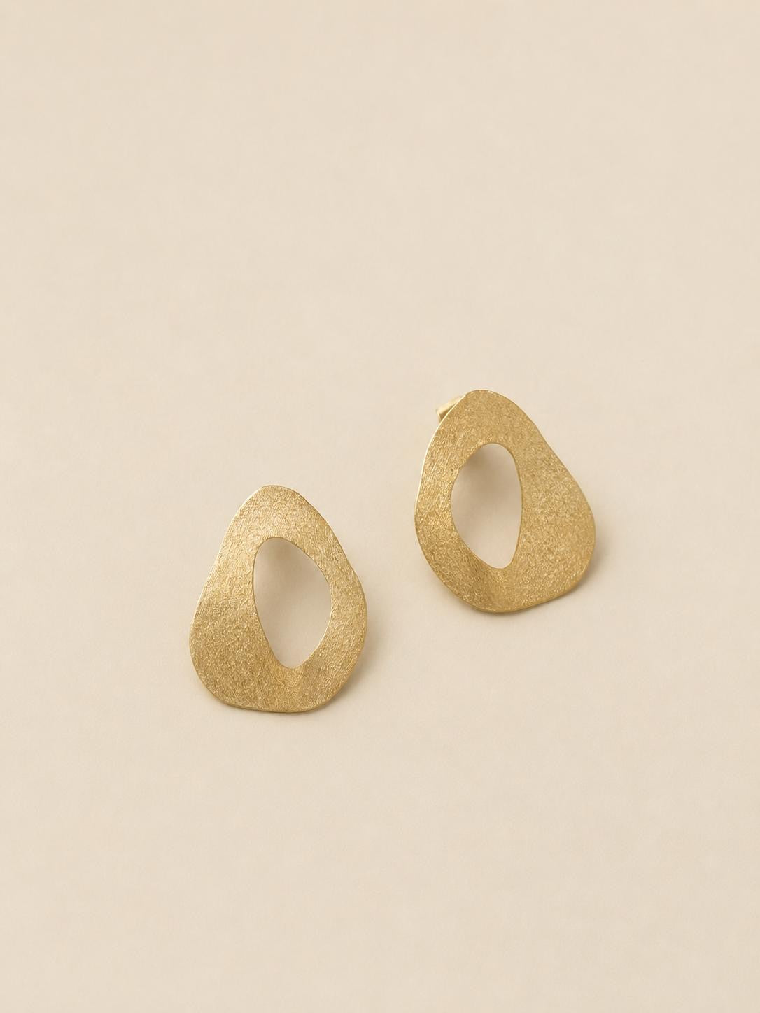 Orecchini Natural Shape RIMA: Caratterizzati da una forma di ispirazione naturale, quasi triangolare e forata al centro, con una silhouette bidimensionale e piatta,  Il design è completato dalla particolare finitura